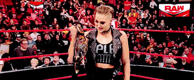 a woman is standing in a wrestling ring holding a trophy while a crowd watches .
