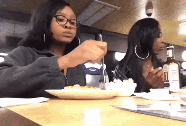two women sitting at a table with a bottle of all sauce