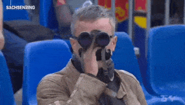 a man sitting in a stadium looking through binoculars with the words sachsenring on the bottom right