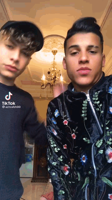 two young men are standing next to each other in front of a chandelier and a sign that says tik tok