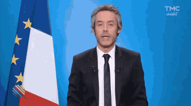 a man in a suit and tie stands in front of a french flag