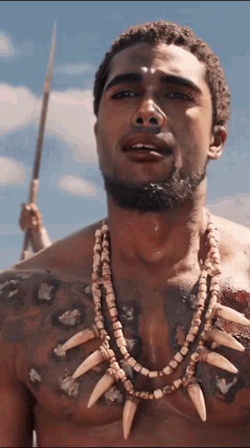 a man wearing a necklace with teeth and a spear in his hand