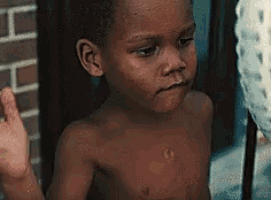 a shirtless young boy is standing in front of a brick building .