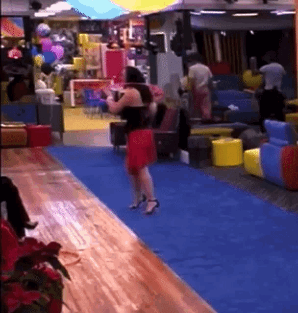 a woman in a red skirt is standing on a blue rug in a room