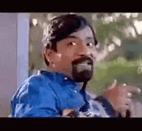 a man with a beard is sitting in front of a window and making a funny face .