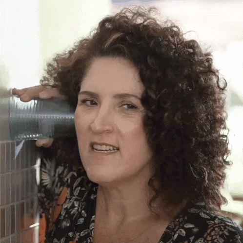 a woman with curly hair is holding a cup in front of her ear