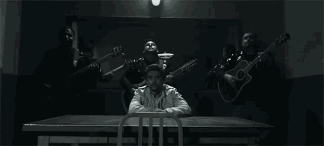 a man sitting at a table with a group of men playing guitars
