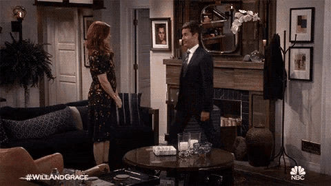 a man in a suit and tie is standing in a living room next to a woman in a dress .