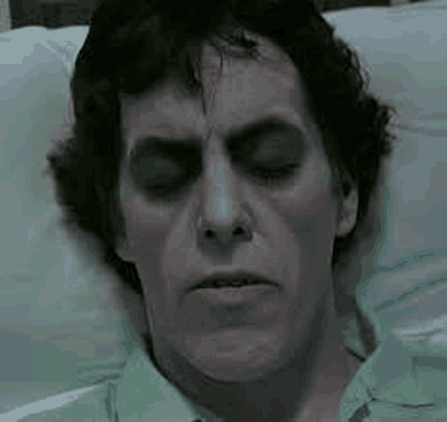 a man is laying in a bed with his eyes closed .