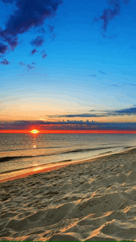 the sun is setting over the ocean and the sand is visible