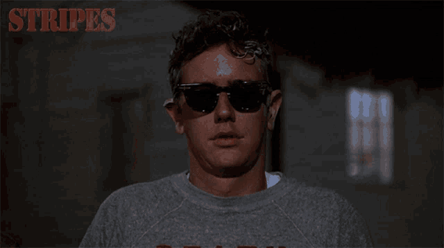 a man wearing sunglasses holds his hand to his forehead with the words stripes behind him