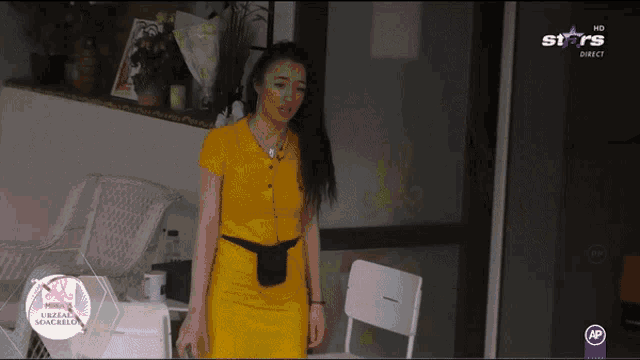 a woman in a yellow dress is standing in front of a tv screen that says stars