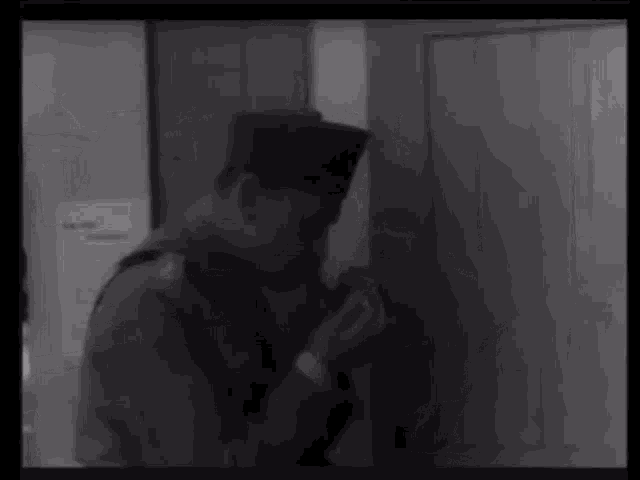 a black and white photo of a man in a military uniform standing in front of a door