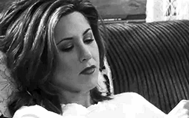 a black and white photo of a woman laying on a couch with her eyes closed .