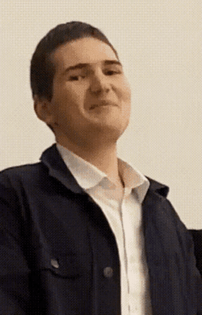 a young man wearing a blue jacket and a white shirt is smiling .
