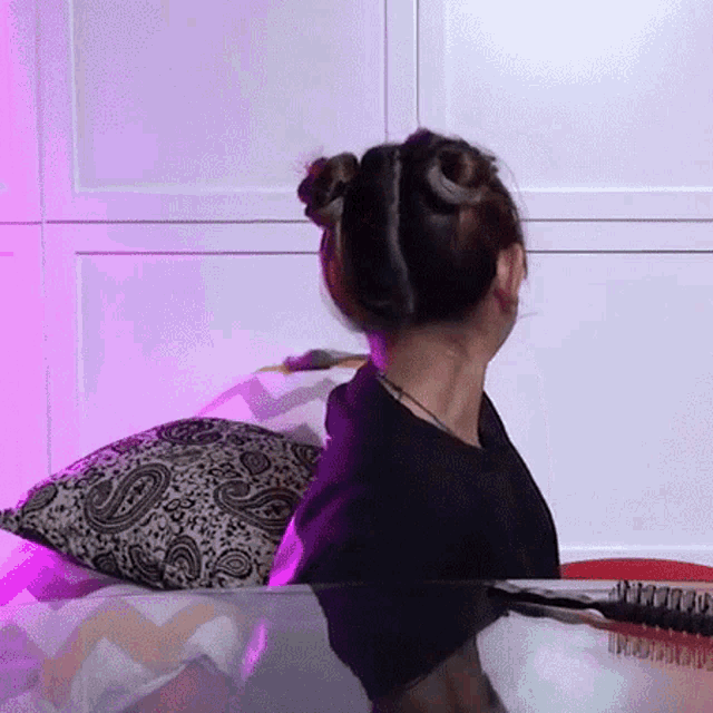 a woman is sitting on a bed with two buns in her hair and a brush .