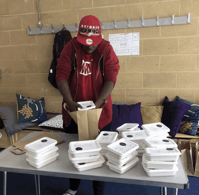 a man wearing a red detroit ducks hat is packing food