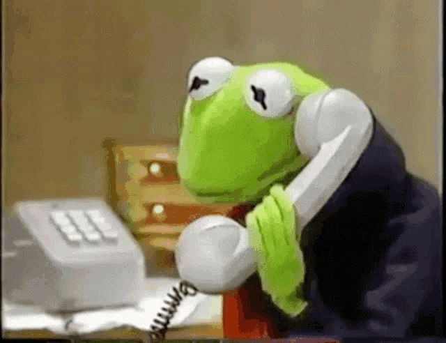 a kermit the frog is talking on a telephone while wearing a tie
