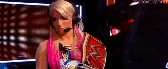 a woman with pink hair is wearing a headset and holding a wrestling championship belt .