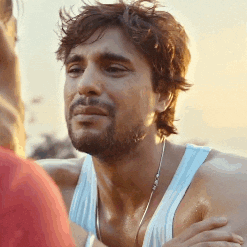 a man with a beard wearing a white tank top looks at a woman