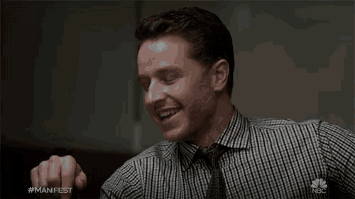 a man wearing a plaid shirt and tie is smiling with the hashtag #manfest on his shirt