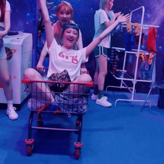 a girl wearing a shirt that says 6r15 is sitting in a shopping cart