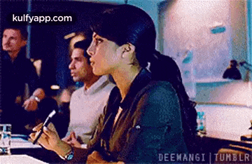 a woman is sitting at a table in front of a group of people holding a pen .