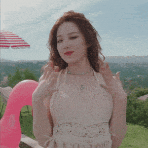 a woman wearing a white top with fringe is standing in front of a pink pool float with the letter o on it