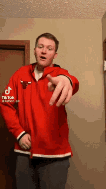 a man wearing a red chicago bulls jacket points at the camera