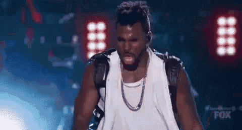 a man is standing on a stage wearing a white tank top and a chain around his neck .
