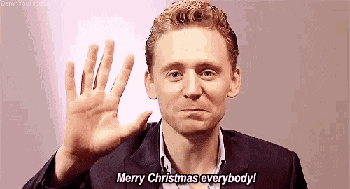 a man in a suit and tie is waving his hand and saying merry christmas everybody .