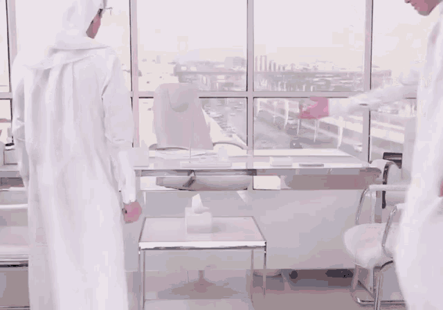 two men in white standing next to each other in front of a window