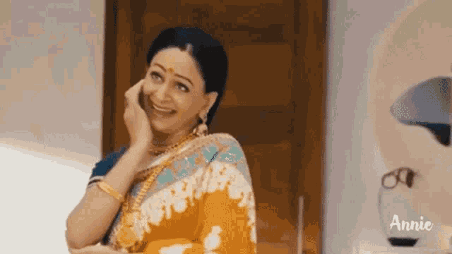 a woman in a saree is talking on a cell phone and smiling .