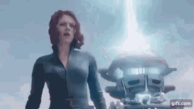 a woman in a black suit is standing in front of a light coming out of a device .