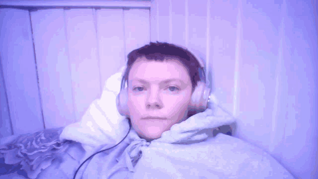 a person wearing headphones and a hoodie laying on a bed