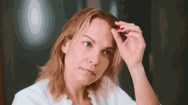 a woman with red nail polish is looking at her hair in the mirror
