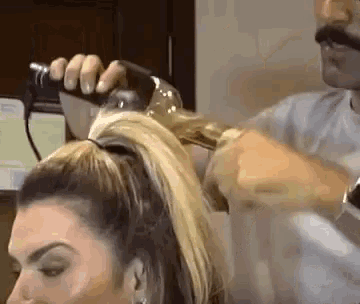a woman is getting her hair done by a man with a blow dryer .