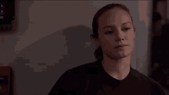 a woman in a black shirt is leaning against a wall next to a fire alarm box .