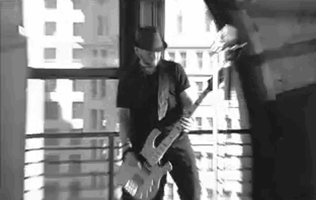 a man is playing a guitar on a balcony in front of a window .
