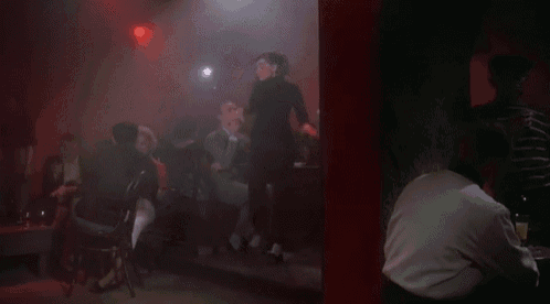 a man is dancing on a stage in a dark room with people sitting at tables in the background .