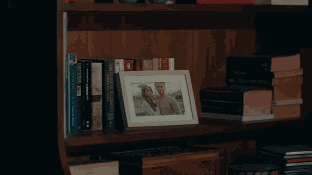 a framed picture of a man and woman sits on a bookshelf next to a stack of books