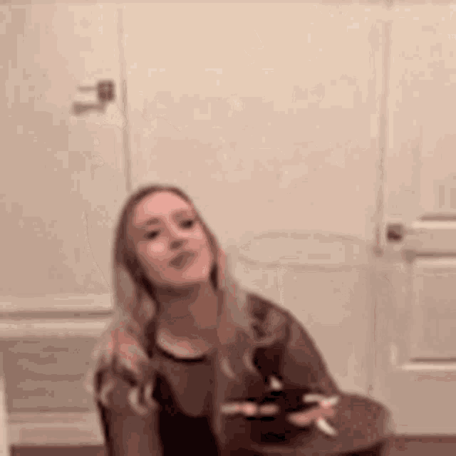 a woman is sitting at a table holding a cell phone and a cigarette .