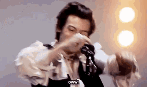 harry styles is crying while holding a microphone and singing into it .