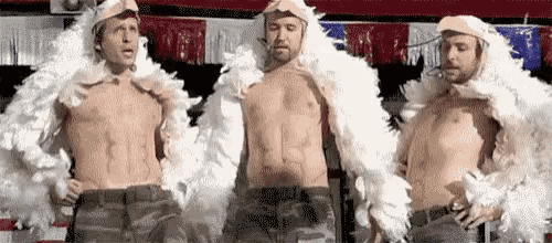 three shirtless men are standing next to each other wearing white feathered jackets and hats .
