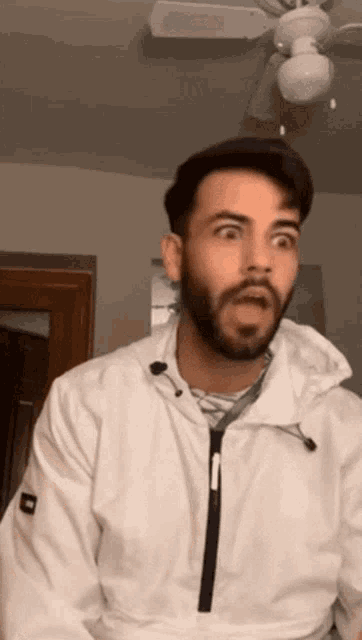 a man with a beard is wearing a white jacket with the letter h on the sleeve