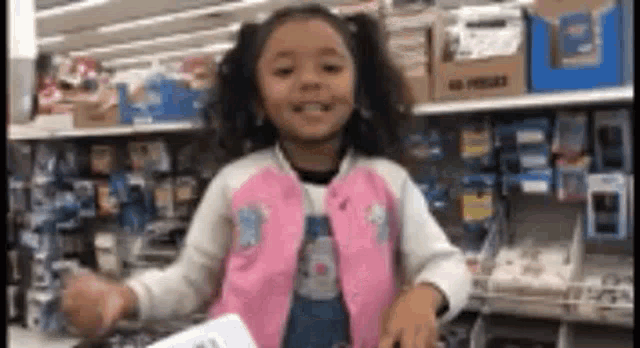 a little girl is standing in front of a shelf in a store and smiling .