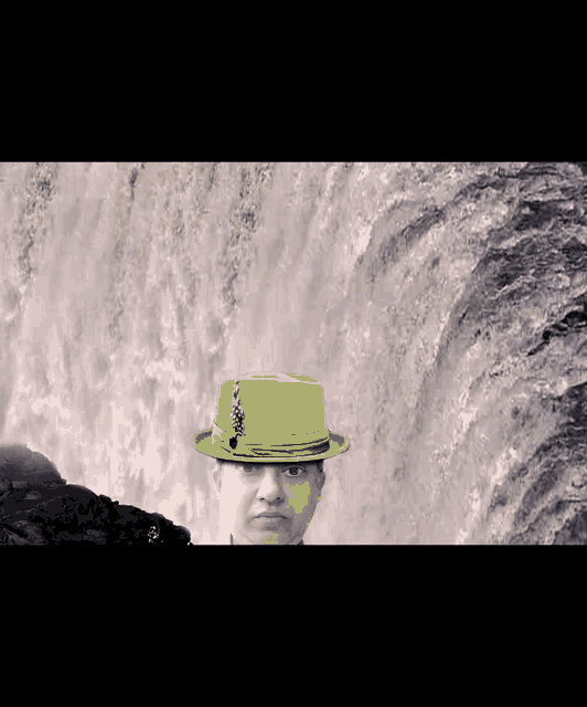 a man wearing a green hat with a waterfall in the background