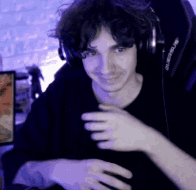a man wearing headphones and a black shirt is sitting in front of a computer screen .