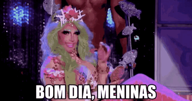 a drag queen says bom dia meninas while wearing a crown