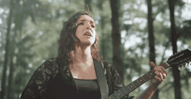 a woman is playing a guitar in the woods with trees in the background
